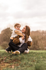 Happy mother with daughter sitting in  park on a grass.Women looking to her baby.