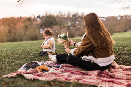 happy mother and child daughter in nature Park on green grass.Mom sitting back to the camera with flower tulpin.