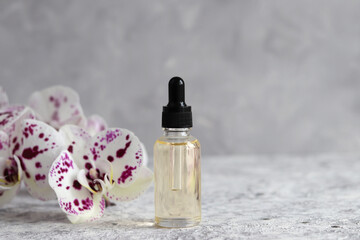 Bottle of cosmetic essential oil with dropper and orchid flowers. Serum skin care products. Beauty concept