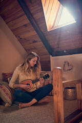 Fototapeta premium Lend me your ear and Ill sing you a song. Shot of a young woman playing the ukelele while relaxing in her bedroom at home.