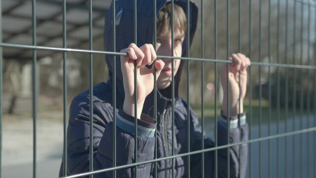 Boy child refugee behind a metal fence. Social problem of war migrants.