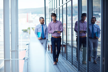 Meeting before their meeting. Shot of two young businessmen using a digital tablet together outside of an office building.