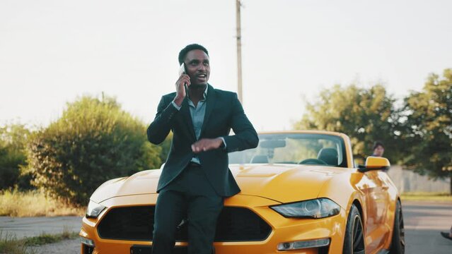 Confident african man in business suit standing near luxury car with modern  smartphone in hands. Handsome male using cell phone while while resting  after a hard day's work.