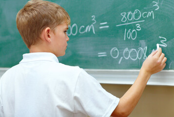 Hes a junior genius. Young schoolboy doing an equation on the blackboard at school. - obrazy, fototapety, plakaty