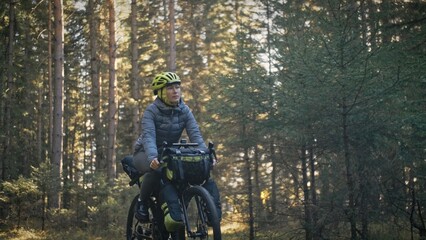 The woman travel on mixed terrain cycle touring with bike bikepacking outdoor. The traveler journey with bicycle bags. Stylish bikepacking, bike, sportswear in green black colors. Magic forest park.