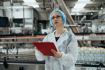 Female worker in protective workwear working in medical supplies research and production factory and checking canisters of distilled water before shipment. Inspection quality control.