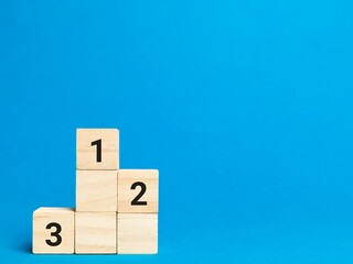 Wooden podium cubes with numbers one two and three against blue background. Achievement concept.