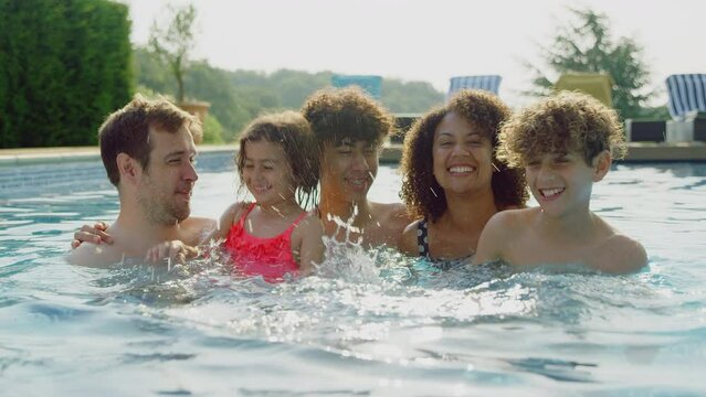 Portrait of multi-racial family relaxing in swimming pool on summer vacation together - shot in slow motion
