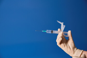 Gloved hand holding syringe on blue background 