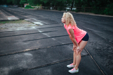 A young curly blonde of athletic build performs a warm-up before training at the stadium. Outdoor...