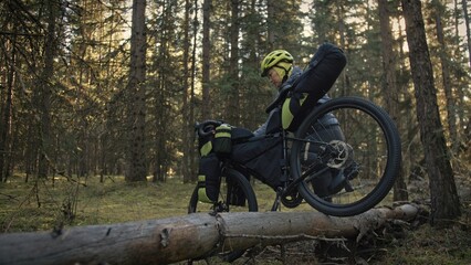 The woman travel on mixed terrain cycle touring with bike bikepacking outdoor. The traveler journey with bicycle bags. Stylish bikepacking, bike, sportswear in green black colors. Magic forest park.