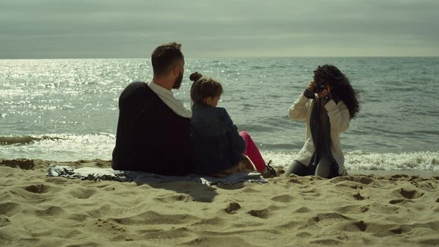 Young family taking pictures on sunny day beach. Mom dad child photographing sea