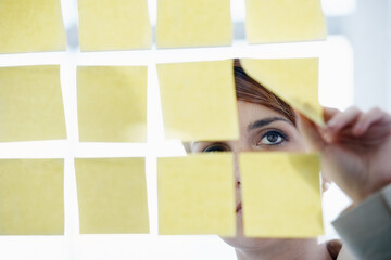 Giving her plans structure. Shot of a businesswoman arranging sticky notes on a glass wal.