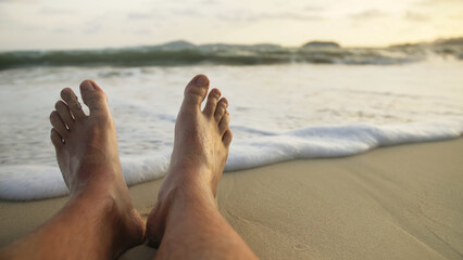 The barefoot man feet relaxed are lying on the sandy beach and washed by the water and foam of the ocean. Concept relax tropical resort traveling happy summer holiday