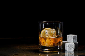 Transparent glass with whiskey and lemon on a dark background.