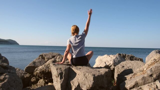 Young caucasian woman doing stretching exercises at the seashore. Girl meditating at the view of the ocean or sea at sunrise. Concept of yoga and solo activity. Meditation and healthy lifestyle.