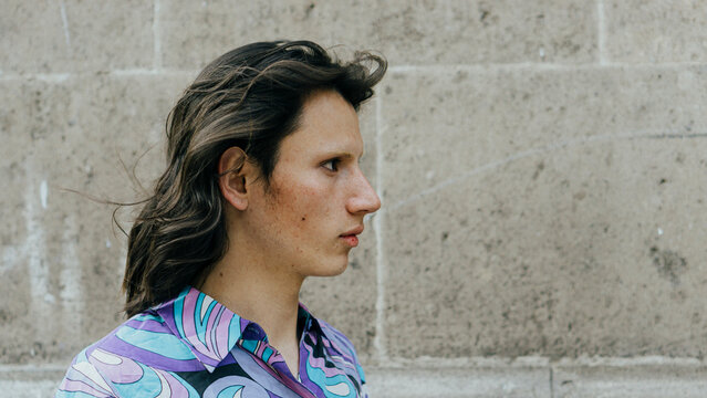 Close-up of a profile of a non-binary person with a brick background.