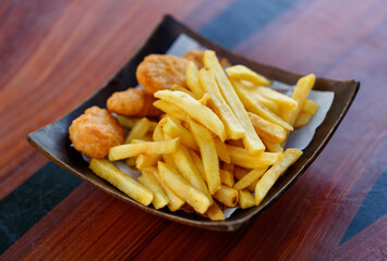 Closeup shot delicious tasty yummy fast junk food snack appetizer pan frying home cooking straight cut french fries and golden crispy chicken meat nuggets in wooden plate placed on wood table counter