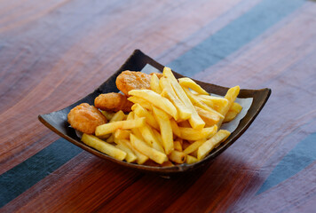 Closeup shot delicious tasty yummy fast junk food snack appetizer pan frying home cooking straight cut french fries and golden crispy chicken meat nuggets in wooden plate placed on wood table counter