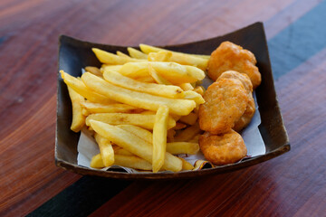Closeup shot delicious tasty yummy fast junk food snack appetizer pan frying home cooking straight cut french fries and golden crispy chicken meat nuggets in wooden plate placed on wood table counter