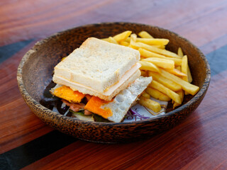 Closeup shot delicious tasty yummy homemade breakfast fried egg, pork bacon and cheese sandwich cutting edge bread with straight cut fresh frying french fries appetizer in wooden bowl on wood table