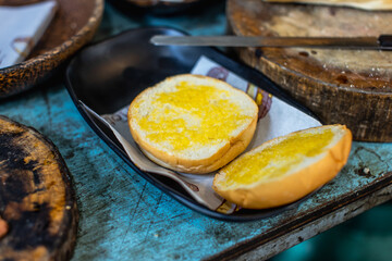 Closeup shot of delicious fresh baked tasty bread and burger bun with sesame topping in old wooden plate placed on round shape wood cutting board on dirty local restaurant counter