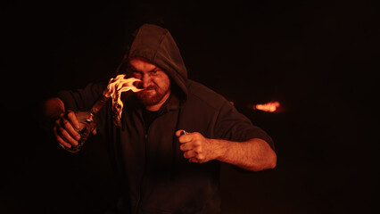 The man in the hood is holding a burning bottle. Molotov cocktail.