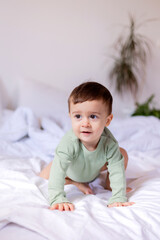 cheerful baby in a green cotton bodysuit is lying on his stomach on a white bed