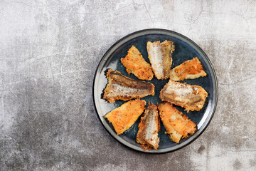 Fried Pollock (hake) fish fillet on a round plate on a dark gray background. Top view, flat lay