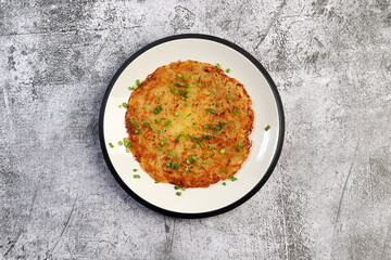 Rustic Potato pancake on a round plate on a dark gray background. Top view, flat lay