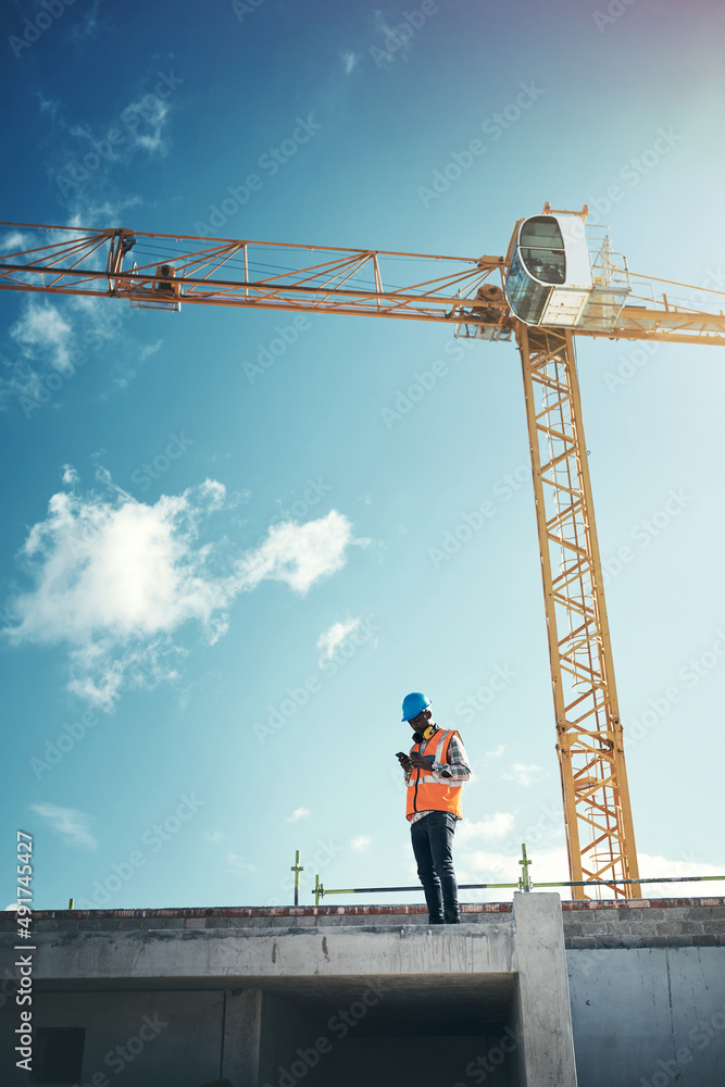 Poster Updating project plans on the go. Shot of a young man using a smartphone while working at a construction site.