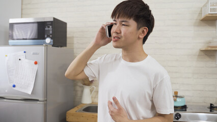 portrait asian male is raising and spreading his arm while talking unhappily on the smartphone in a home interior with white brick wall.