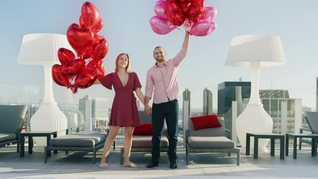 Slow motion beautiful young romantic couple with bunch huge red hearts balloons 