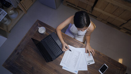 top view woman working overtime from home is adding number on the calculator and taking down the...