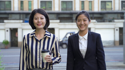 attractive entrepreneur looking at the camera with confident smile is tucking her hair while moving on side by side with her business partner outdoors