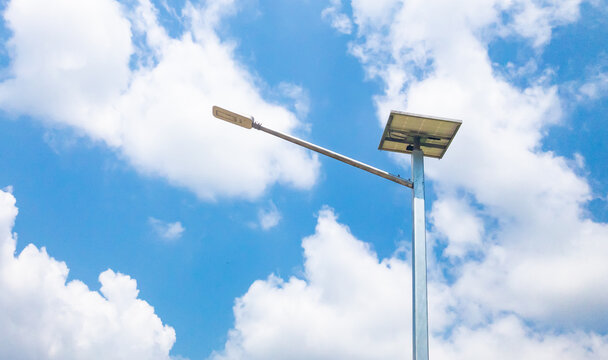 The picture of a lamp pole illuminated during the day is using solar generators from solar panels technology as clean energy against a blue sky background with bright white clouds.