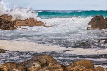 Waves breaking over coastal rocks withy green wave in background