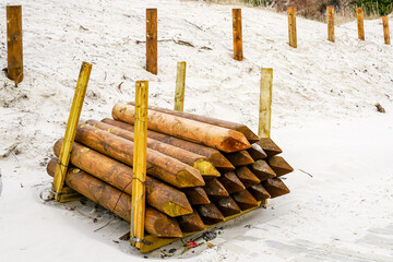 stack of thick round natural wooden fence posts with a sharpened end in the beach dune area