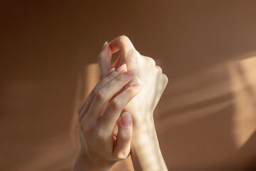 Beautiful female hands apply cream, lotion to skin. Close-up, beige background with striped shadow....