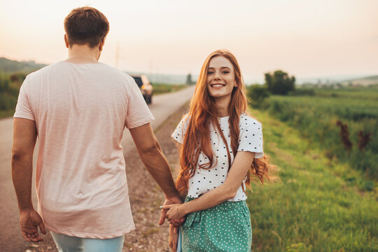 Man and woman walking on the side of the road holding hands, woman turning her face to the camera, smiling. Beautiful young girl. Summer vacation. Pretty young
