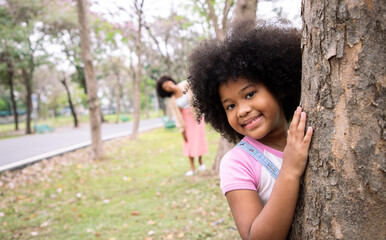 Mother and daughter play hide and seek behind tree with bright smiling in the park. Family leisure...