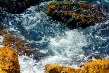 	
Foamy Mediterranean sea hitting rocky shore during hot summer day.