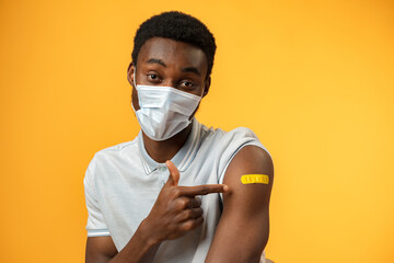 Vaccinated african american man showing his arm against yellow background