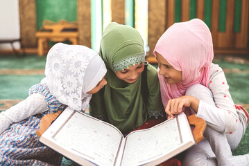 Group of a children reading a holy book Quran in the mosque. Happy Muslim family. Muslim girls in...