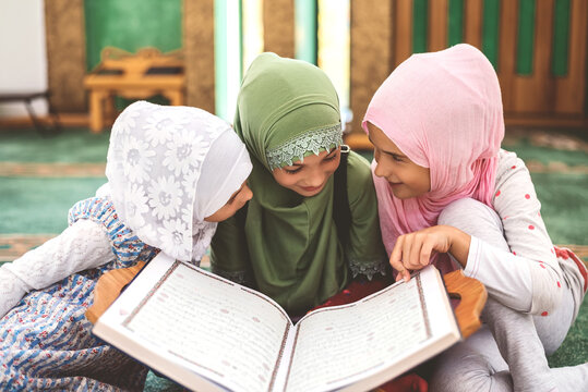 Group of a children reading a holy book Quran in the mosque. Happy Muslim family. Muslim girls in hijab studying Islam religion. 