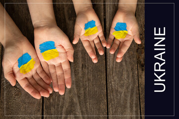 Hands of a mother and a child with a painted yellow-blue flag of Ukraine on a wooden background....