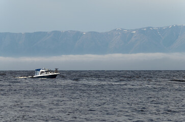 The boat floats on the lake against the background of mountains and fog.