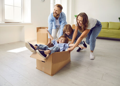 Overjoyed young Caucasian family with small children have fun ride in boxes on moving day to new home. Smiling parents with little kids celebrate relocation to own house. Ownership, rental, realty.