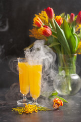 Cocktail of mimosis with steam, a bouquet of tulips on the table. Spring holiday