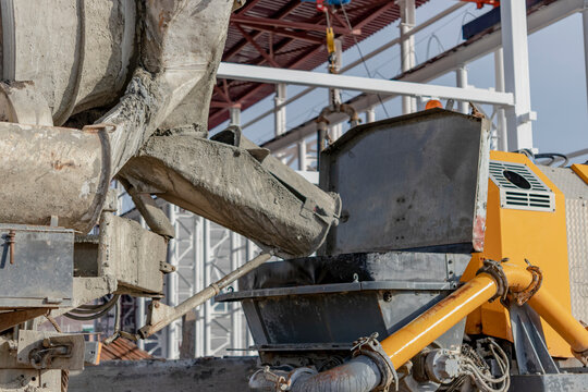 A concrete mixer truck pours mortar into a concrete pump at a construction site. Supply of concrete and mortar for the production of monolithic reinforced concrete works. Close-up.